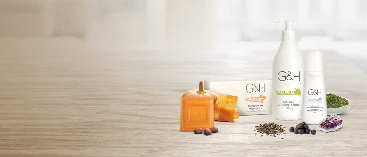 Productos G&H para el cuidado corporal rodeando los productos hay nueces, una calabaza pequeña, semillas de uva, arándanos, polvo de té verde, un cristal de amatista y hojas secas de té blanco. Ingredientes inspirados en la naturaleza.